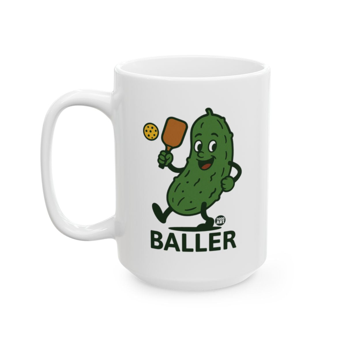 White ceramic mug featuring a pickle character holding sports equipment with the word “Baller,” designed by Todd Art